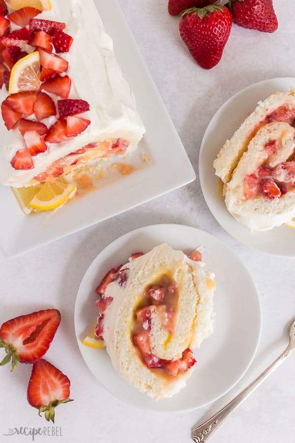 strawberry lemon angel food cake roll overhead with two slices on white plates and a fresh strawberry