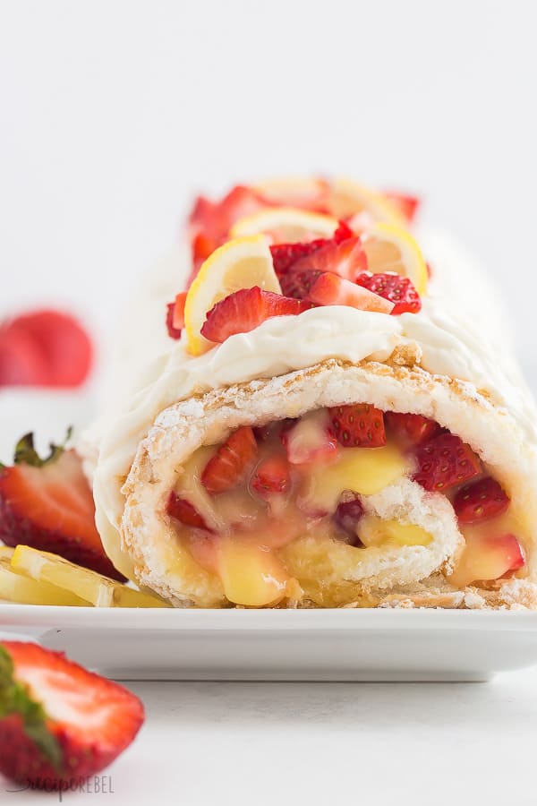 This Strawberry Lemon Angel Food Cake Roll is an easy dessert made with angel food cake mix, fresh lemon curd, and loads of fresh strawberries! The perfect summer dessert! #strawberry #lemon #dessert #cake #recipe strawberry lemon cake roll close up with fresh strawberries and lemon wedges on top