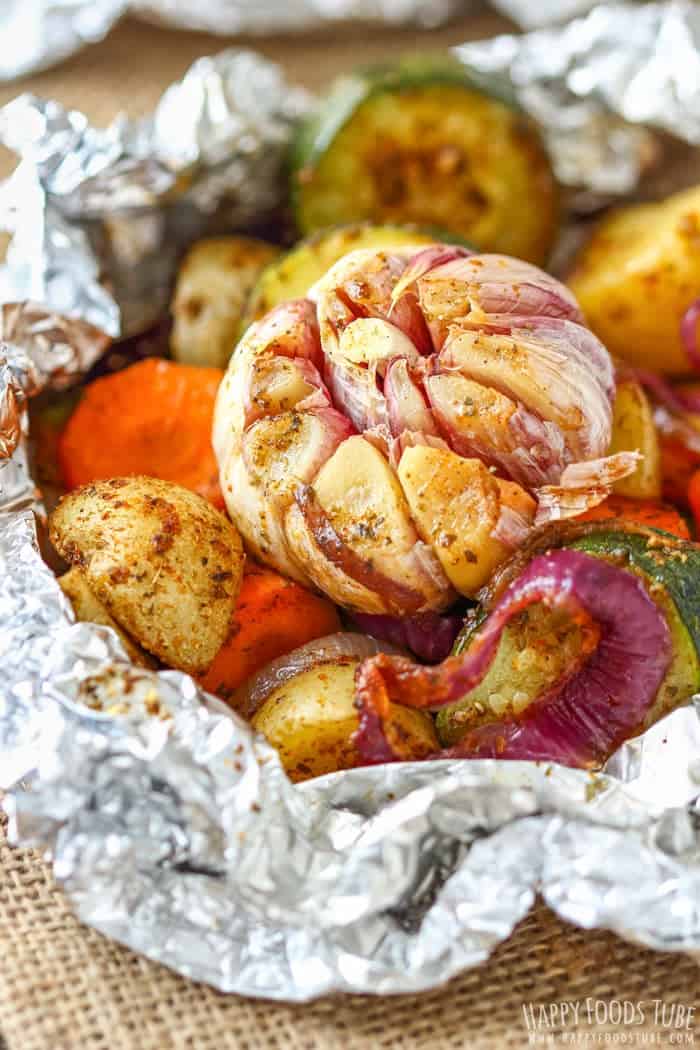 vegetable foil packs with head of garlic on top with potatoes and zucchini