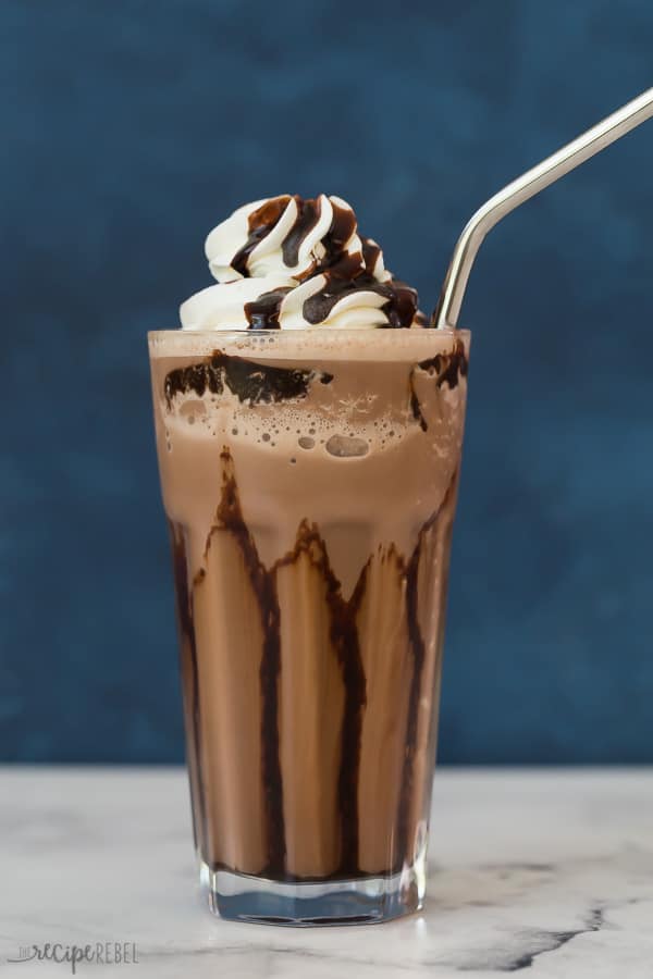 classic frozen hot chocolate in glass with stainless steel straw against a blue background