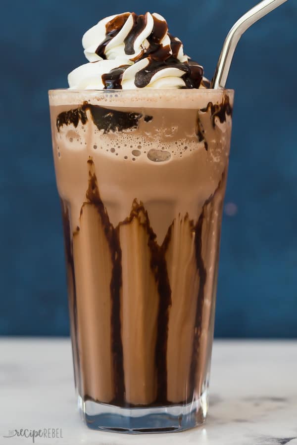 frozen hot chocolate with whipped cream and chocolate drizzle against a blue background