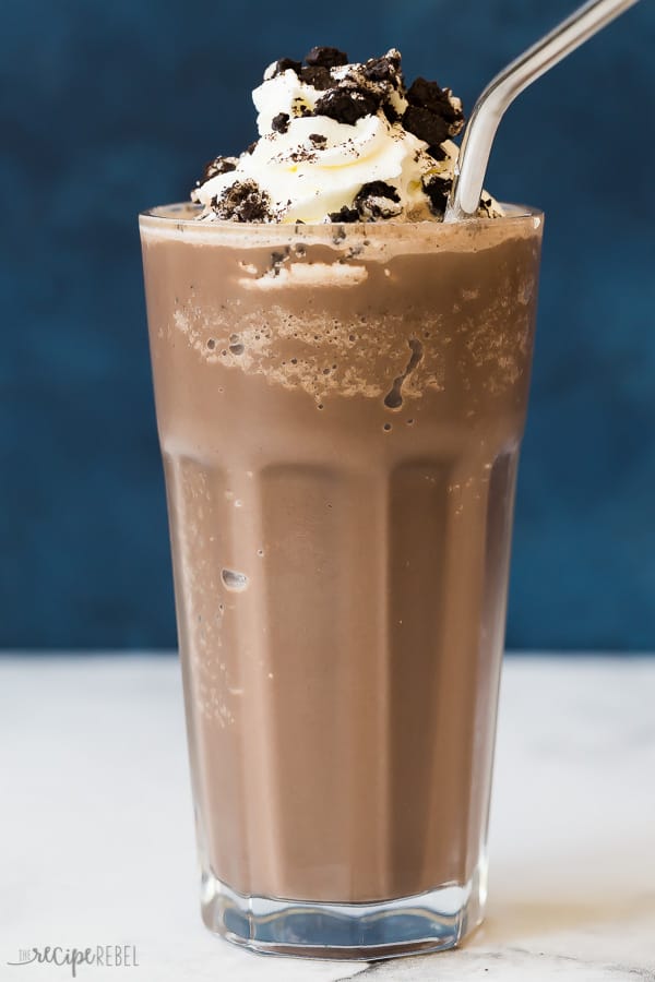 Oreo frozen hot chocolate in glass with oreo crumbles against a blue background