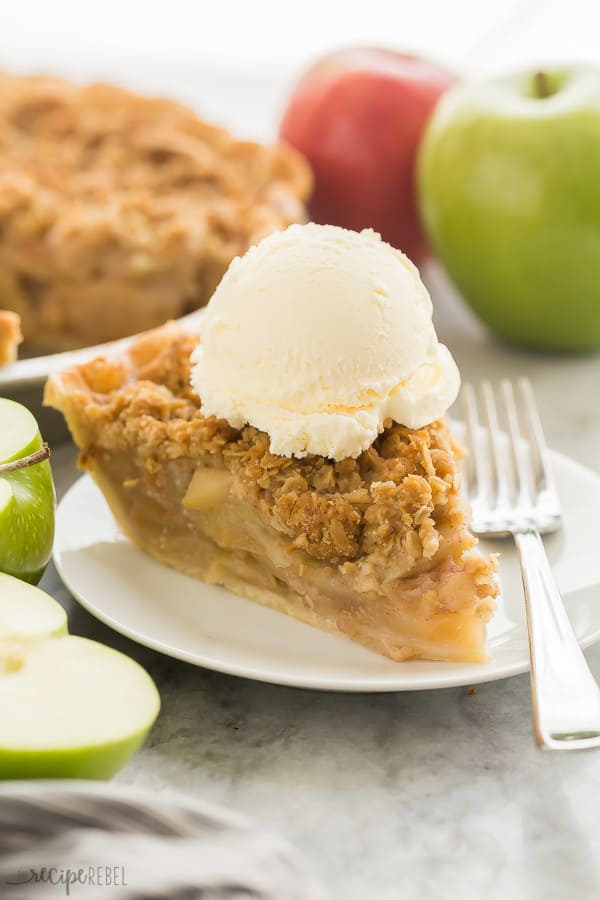 apple crumble pie slice on white plate with ice cream and apples in the background