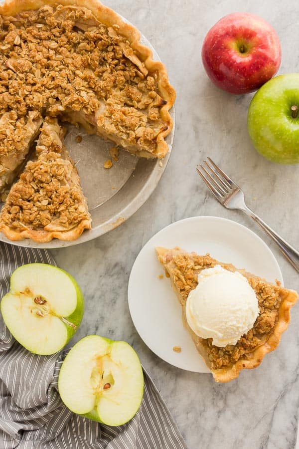 apple crumble pie overhead with slice on white plate and the rest in tin ppie plate and halved apple