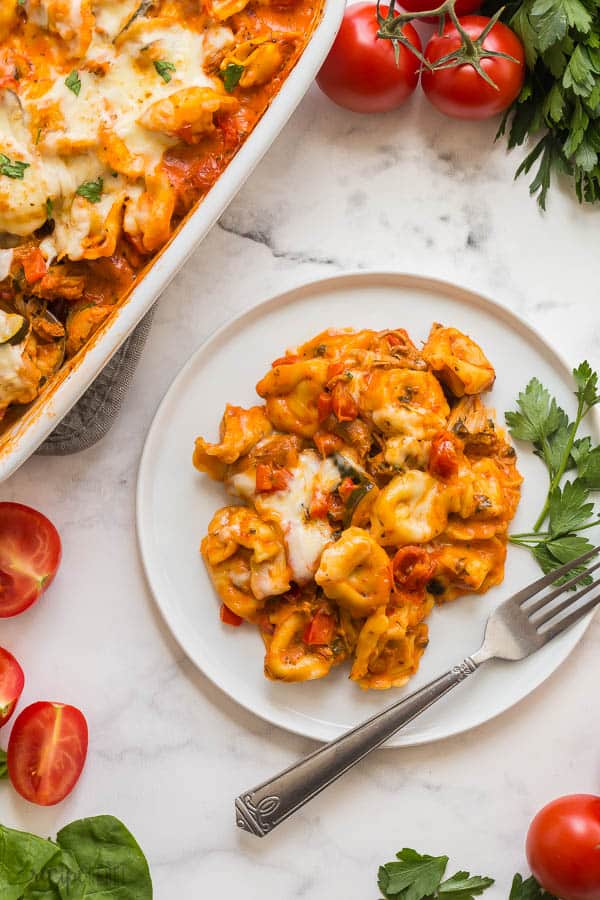 baked cheese tortellini on white plate with fresh parsley and fork