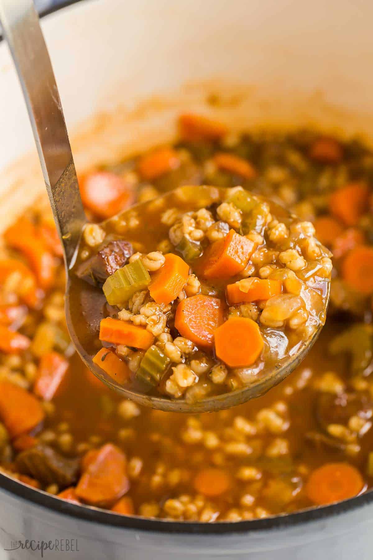 This easy Beef Barley Soup is a hearty, healthy soup recipe that is made with tender chunks of beef, loads of vegetables and pearl barley. Make ahead and freezer friendly. #beef #soup #recipe | easy soup recipes | healthy soup | beef roast | steak recipes | beef recipes | comfort food | healthy meals a metal ladle scooping beef barley soup from dutch oven.