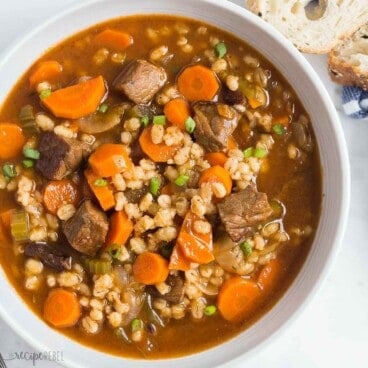 square image of a bowl or beef barley soup with fresh chopped parsley.