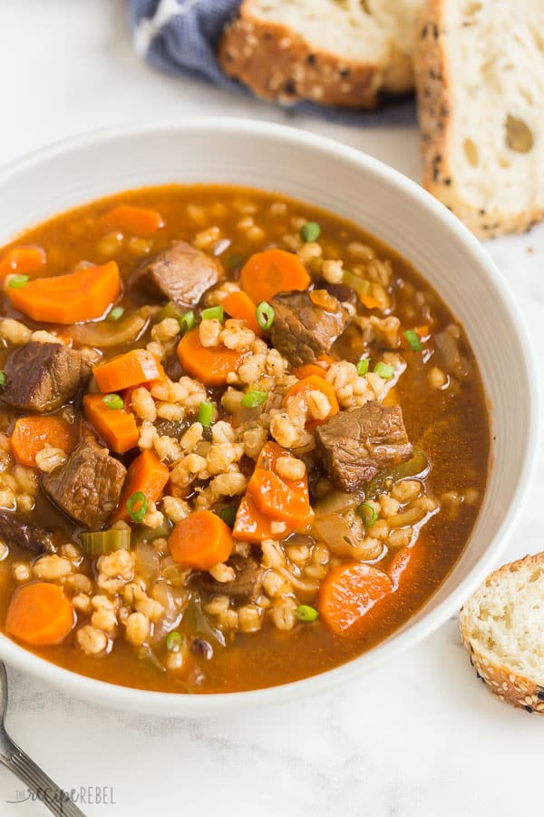 beef barley soup in bowl close up on white background with crusty bread