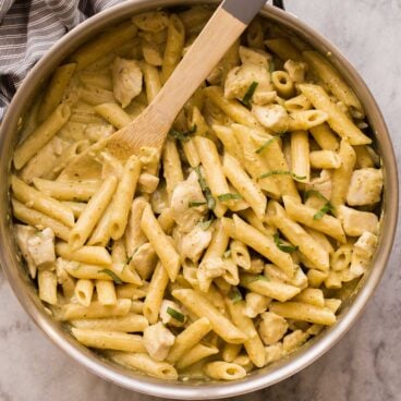 overhead image of chicken pesto pasta in skillet with wooden spoon