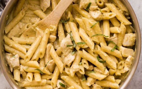 overhead image of chicken pesto pasta in skillet with wooden spoon