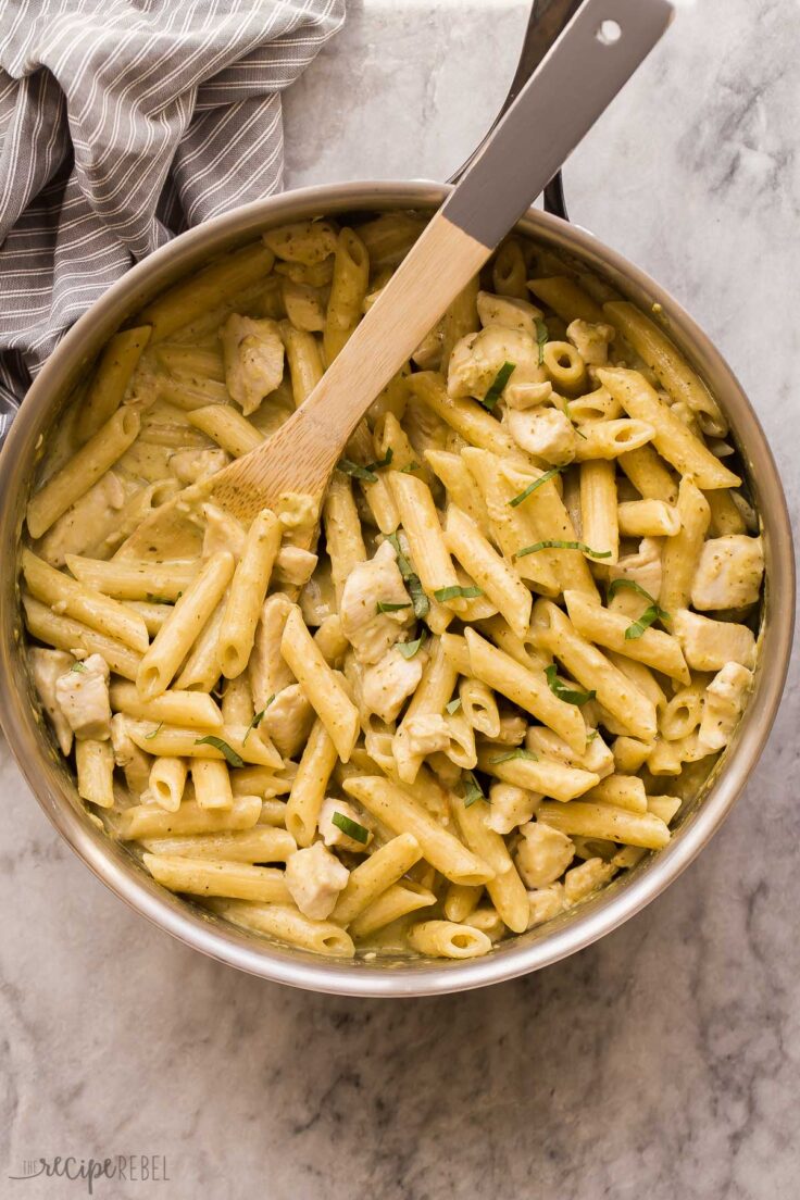 overhead image of chicken pesto pasta in skillet with wooden spoon