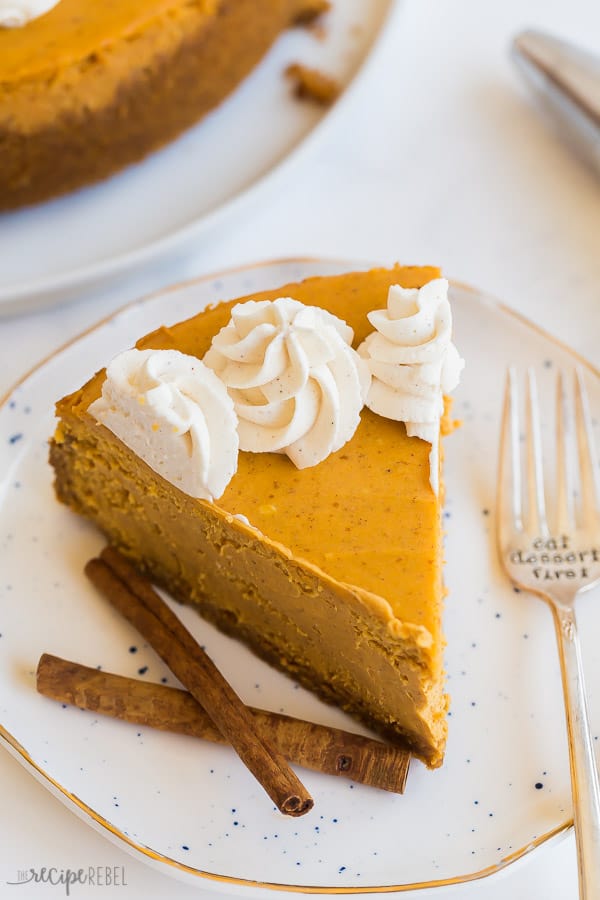 pumpkin cheesecake slice close with whipped cream swirls cinnamon sticks and fork