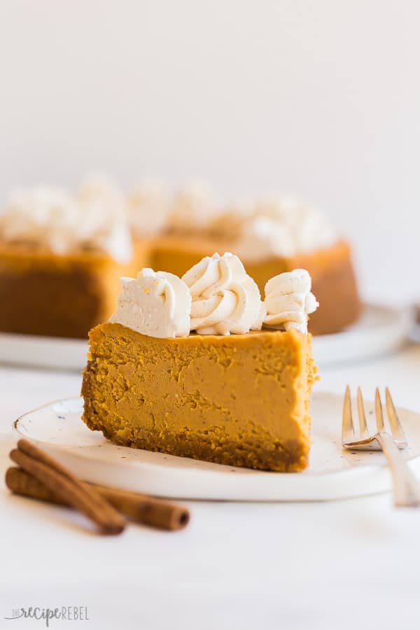 pumpkin cheesecake slice on white plate with fork and cinnamon sticks