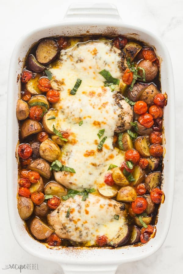 caprese chicken with potatoes in white baking dish with cherry tomatoes and mozzarella cheese