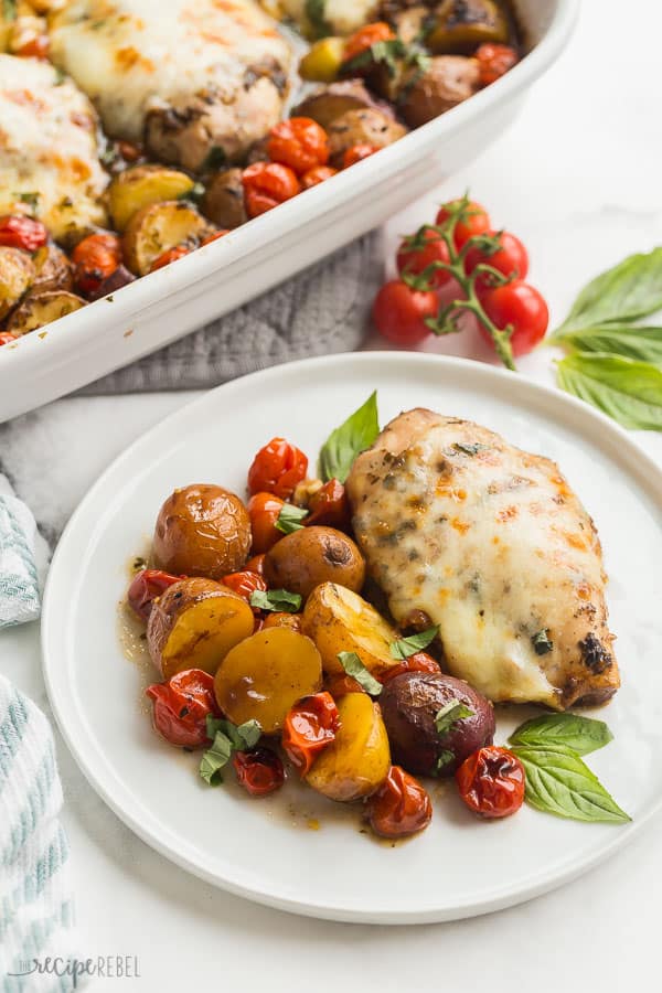 caprese chicken plated on white plate with baking dish in background and fresh tomatoes