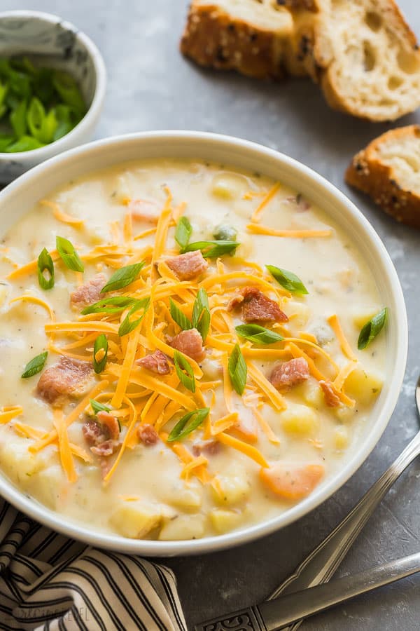 slow cooker potato soup in bowl close up in white bowl on grey background with crusty bread