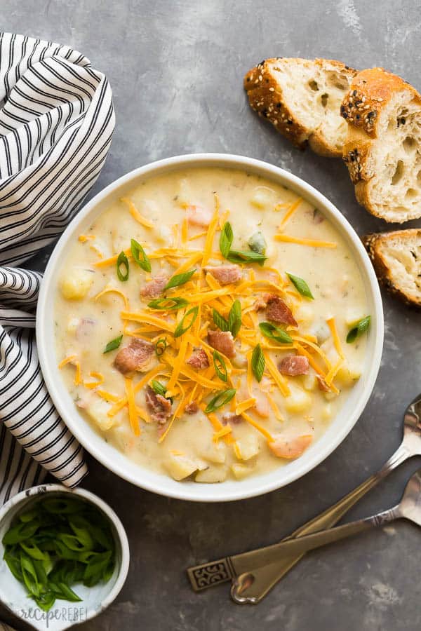 crockpot potato soup in bowl overhead with crusty bread, green onions and striped towel in the background