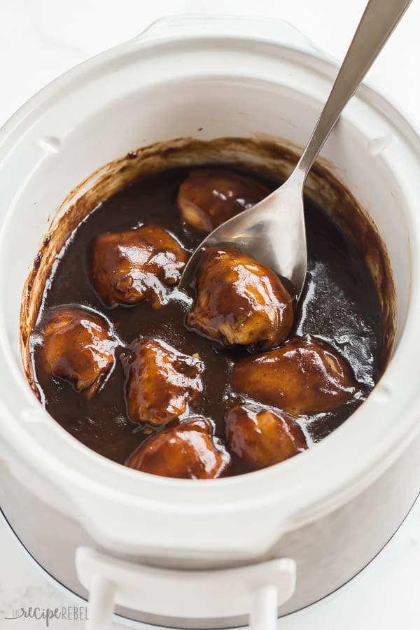 These Crock Pot Chicken Thighs with Honey Balsamic glaze are sweet and sticky with just the right amount of tang and spice! A melt in your mouth tender, crockpot dump meal that the whole family will love! #crockpot #slowcooker #chicken #chickenthighs #dinner #recipe crockpot chicken thighs in slow cooker with thick balsamic glaze and metal spoon