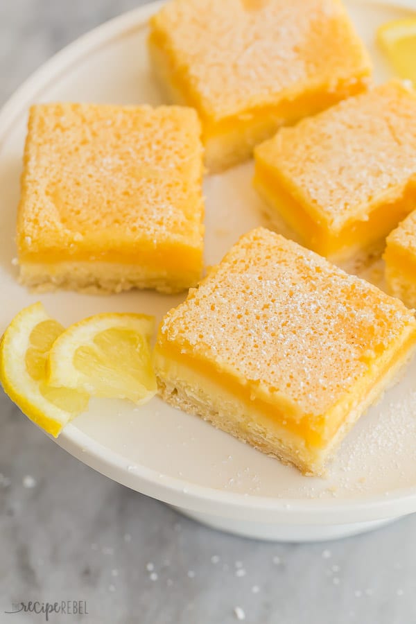 lemon bars on white plate close up with lemon wedges on marble background