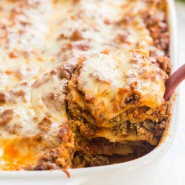 piece of lasagna being scooped out of white baking dish.