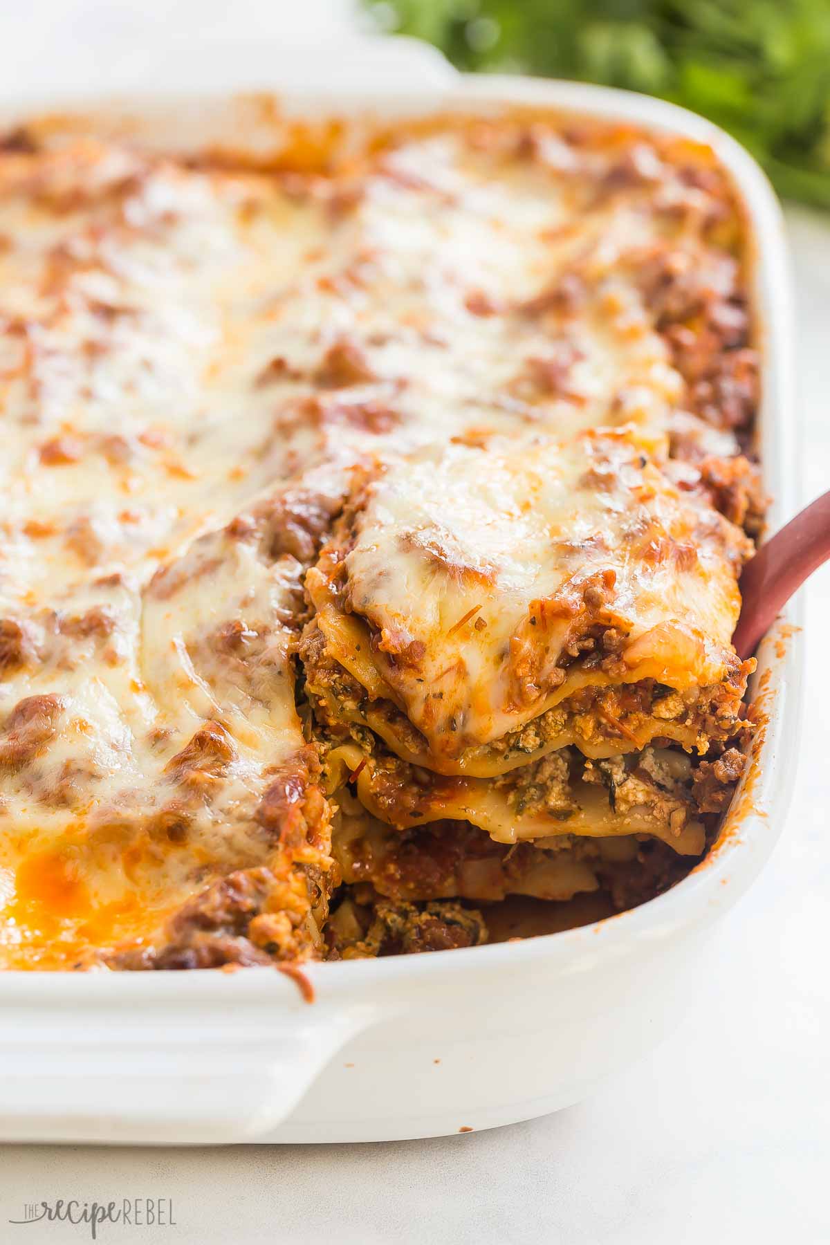 piece of lasagna being scooped out of white baking dish.