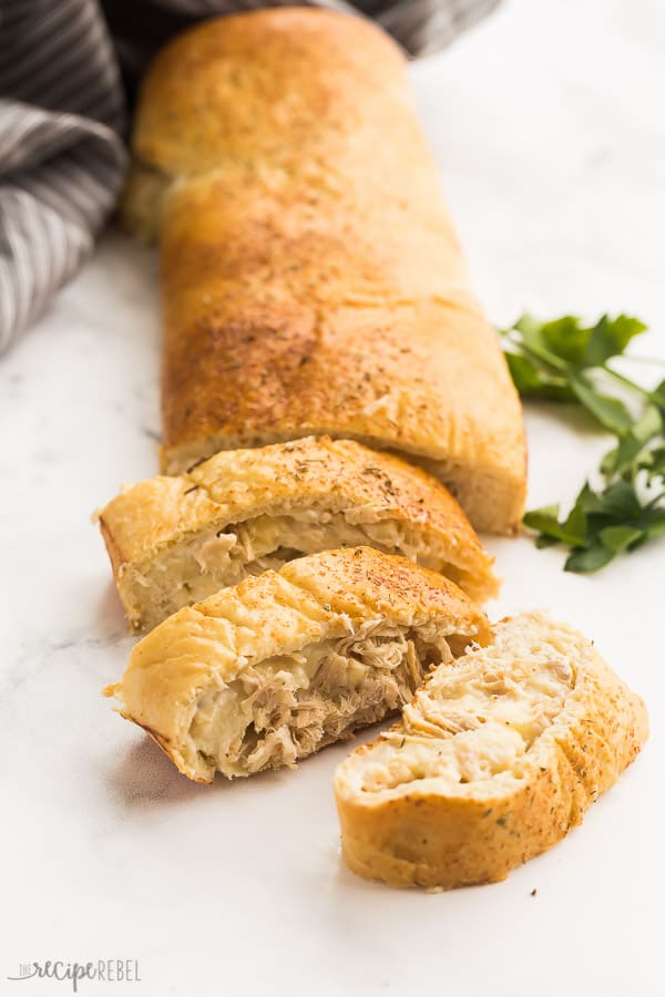 This Turkey Alfredo Stromboli is an easy meal that includes leftover turkey, homemade Alfredo sauce, and cheese, rolled up in pizza dough and baked until golden! Perfect for an easy dinner or school lunches. #turkey #dinner #recipes #easyrecipe turkey alfredo stromboli sliced with grey towel and fresh parsley in the background