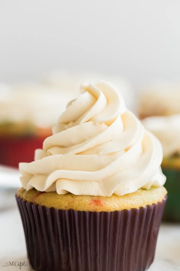 vanilla buttercream frosting close up on sprinkle cupcake with purple liner