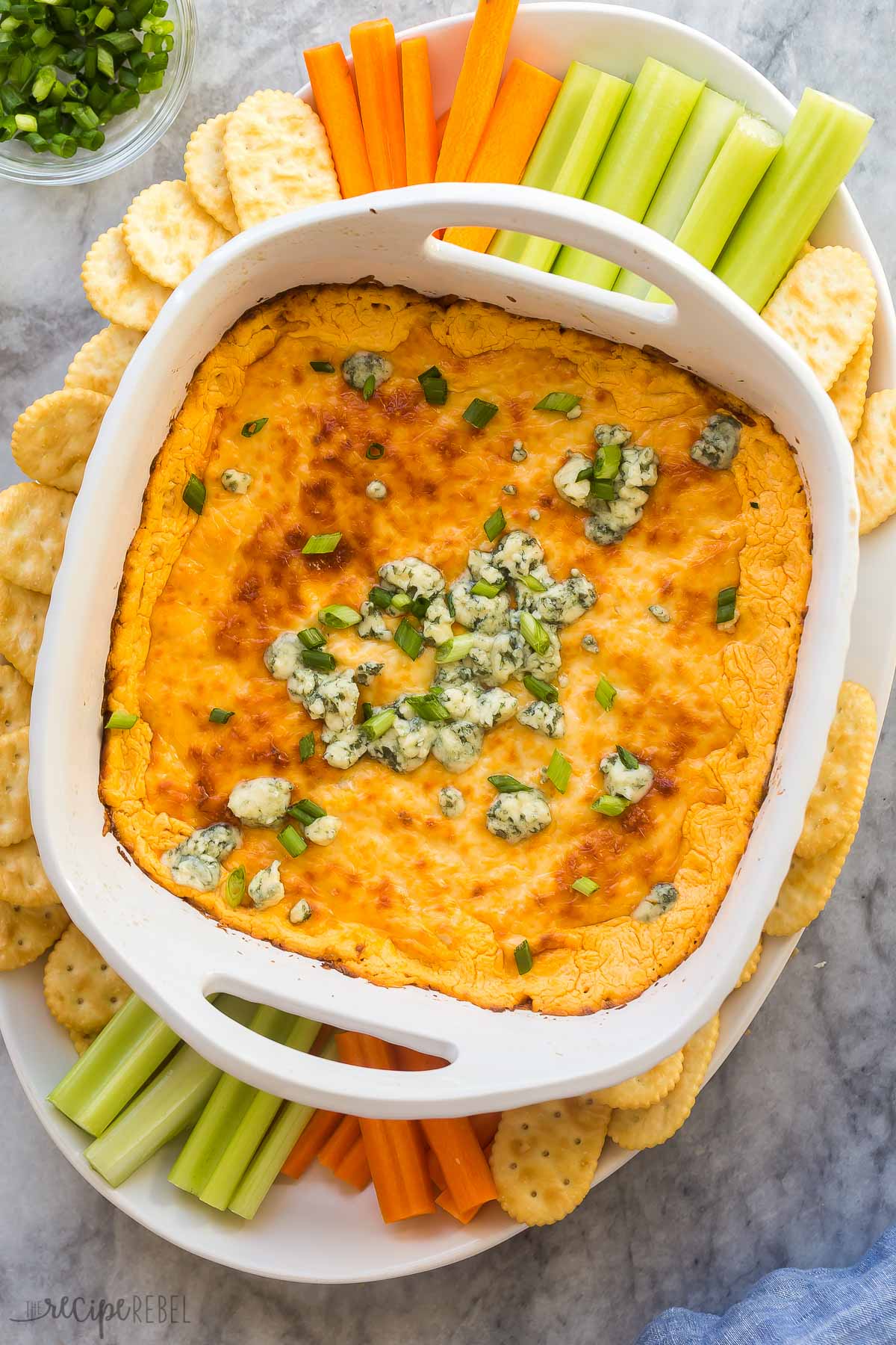 overhead image of buffalo chicken dip in white casserole dish with veggies around