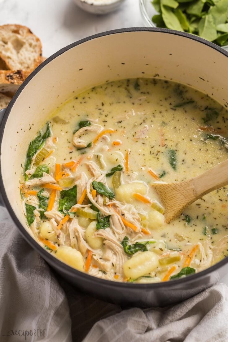 This Chicken Gnocchi Soup is better than Olive Garden! Loaded with tender chicken, chunks of vegetables, and spinach in a creamy, flavorful broth, it's made in 30 minutes! #soup #recipes #dinner | easy dinner ideas | easy recipes | chicken breast | chicken dinners | healthy soup close up image of wooden spoon stirring chicken gnocchi soup