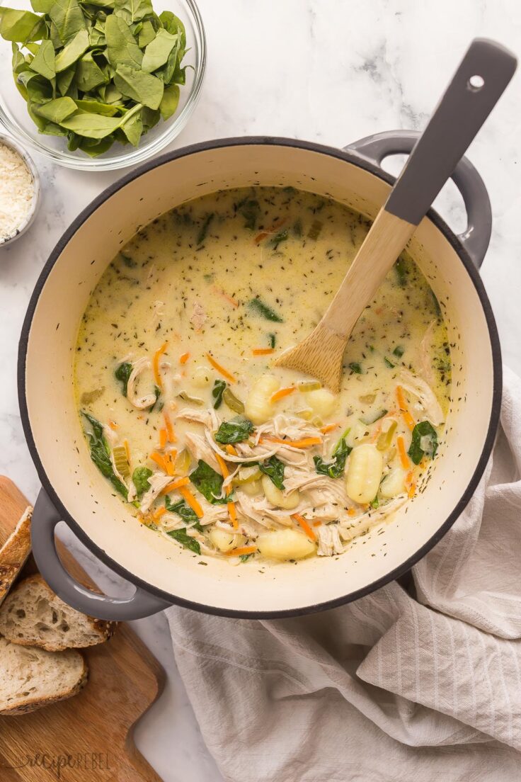 This Chicken Gnocchi Soup is better than Olive Garden! Loaded with tender chicken, chunks of vegetables, and spinach in a creamy, flavorful broth, it's made in 30 minutes! #soup #recipes #dinner | easy dinner ideas | easy recipes | chicken breast | chicken dinners | healthy soup overhead image of pot of chicken gnocchi soup with wooden spoon