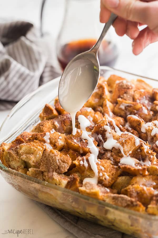 french toast casserole in glass pan with glaze drizzle from a spoon