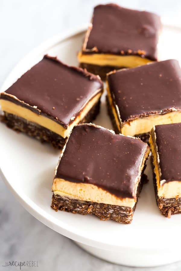 nanaimo bars cut into pieces on white plate on white marble background