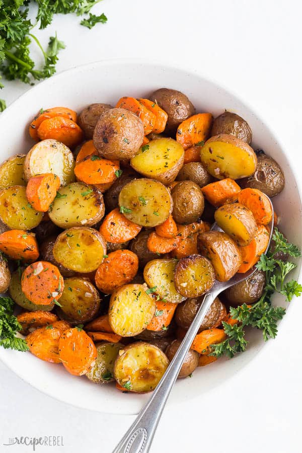 A white serving dish full of roasted potatoes and carrots, garnished with fresh parsley sprigs.