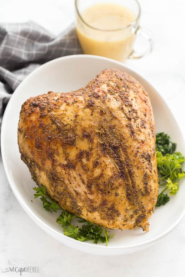 This Sous Vide Turkey Breast is a foolproof way to get juicy turkey! Well seasoned, with crispy, browned skin and served with apple cider gravy! With step by step video. #turkey #sousvide #recipe #dinner #thanksgiving #christmasdinner sous vide turkey breast bone in on white plate with parsley and grey towel