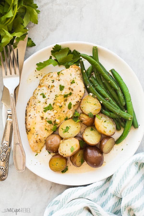 This Slow Cooker Garlic Butter Chicken and Potatoes is an easy hands-off meal with just 5 minutes prep time! Juicy chicken breasts and tender potatoes in a garlic butter sauce. With step by step recipe video down below! #crockpot #slowcooker #chickenbreast #dinner #recipes slow cooker chicken and potatoes on white plate with fresh parsley