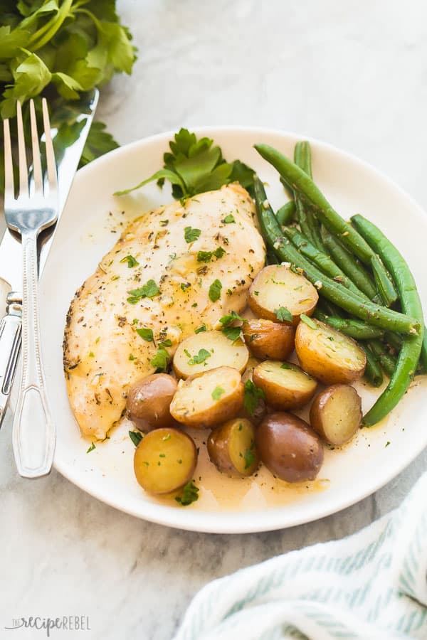 This Slow Cooker Garlic Butter Chicken and Potatoes is an easy hands-off meal with just 5 minutes prep time! Juicy chicken breasts and tender potatoes in a garlic butter sauce. With step by step recipe video down below! #crockpot #slowcooker #chickenbreast #dinner #recipes garlic butter chicken and potatoes on plate with marble background