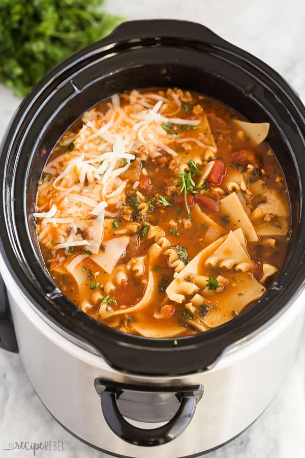 crockpot lasagna soup in black slow cooker with shredded cheese on top