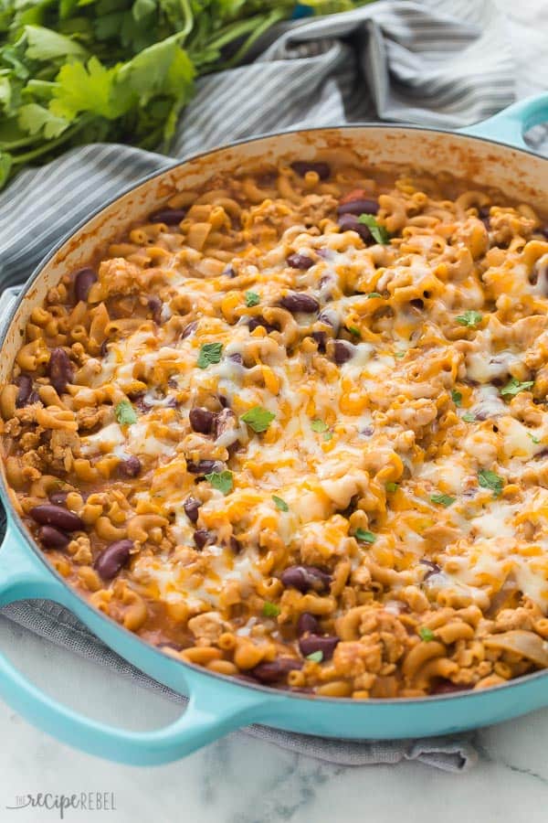 This Turkey Chili Mac and Cheese is a hearty, healthy one pot pasta that comes together in 30 minutes or less! With step by step recipe video. #dinner #recipes #turkey #pasta #macaroni turkey chili mac in blue braiser with melted cheese on top and grey towel in the background