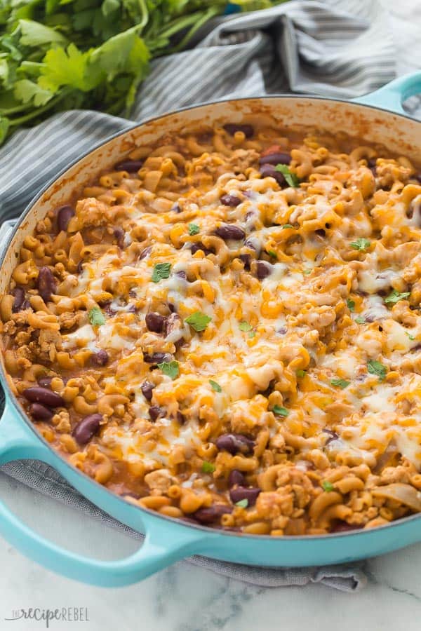 turkey chili mac in blue braiser with melted cheese on top and grey towel in the background