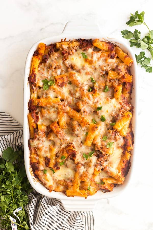 Baked Ziti with Italian Turkey Sausage is a hearty, make ahead casserole that's family and freezer friendly! A healthier twist with all of the same incredible flavor! #pasta #dinner #recipes baked ziti with italian sausage in white casserole dish with fresh parsley