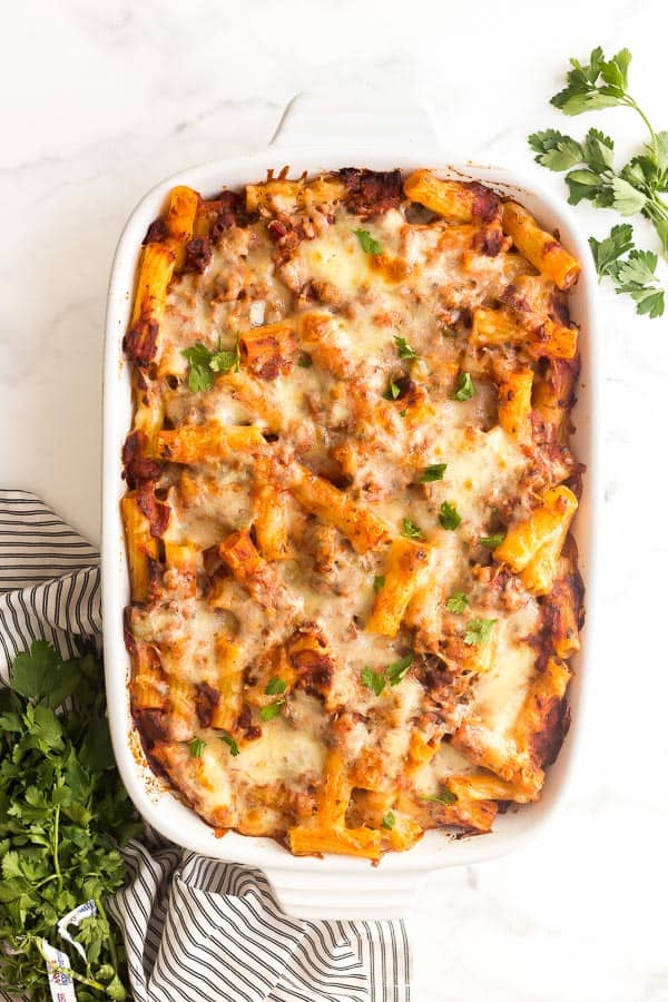 baked ziti with italian sausage in white casserole dish with fresh parsley