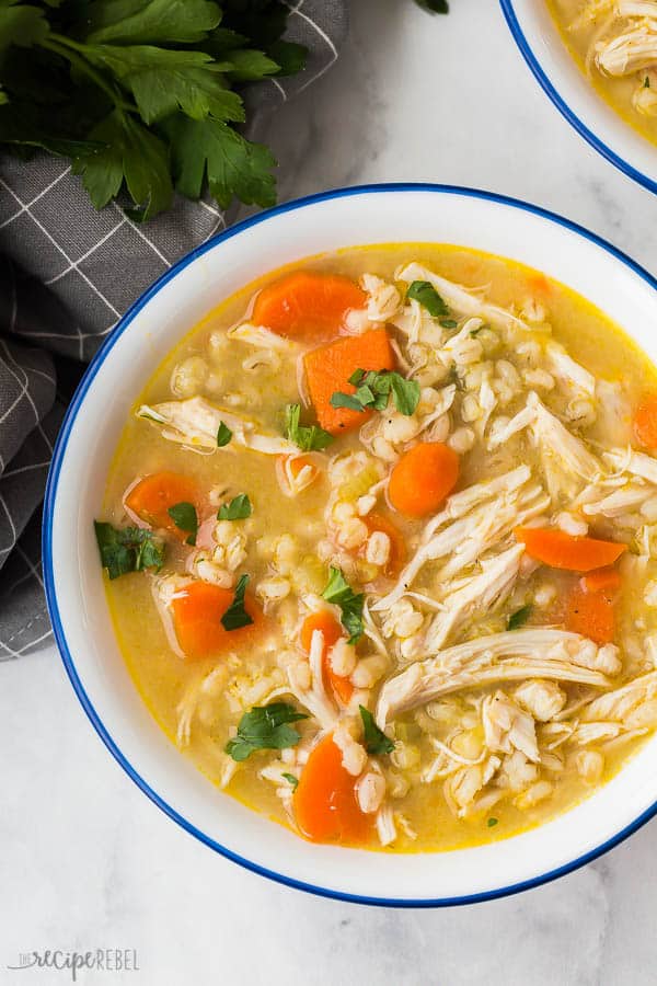 chicken barley soup close up in white bowl with blue rim