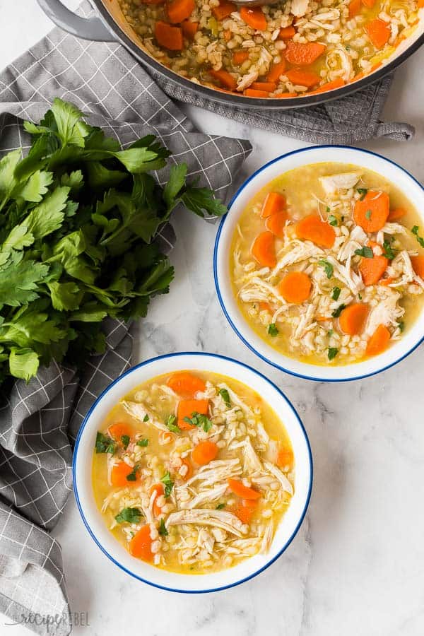 chicken barley soup two bowls with blue rim on white marble background