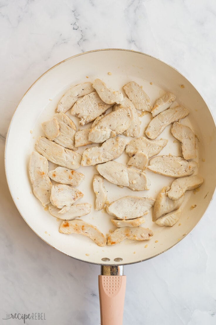 sliced chicken breasts cooking in white skillet