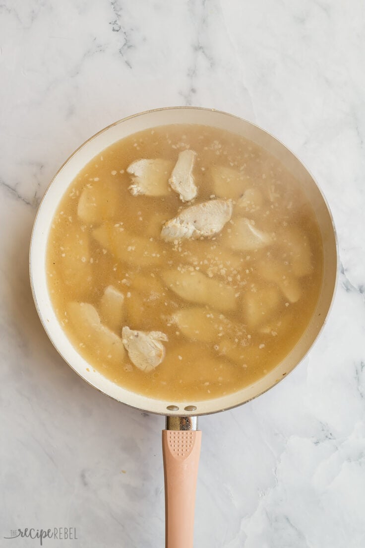 broth added to chicken breasts in white skillet