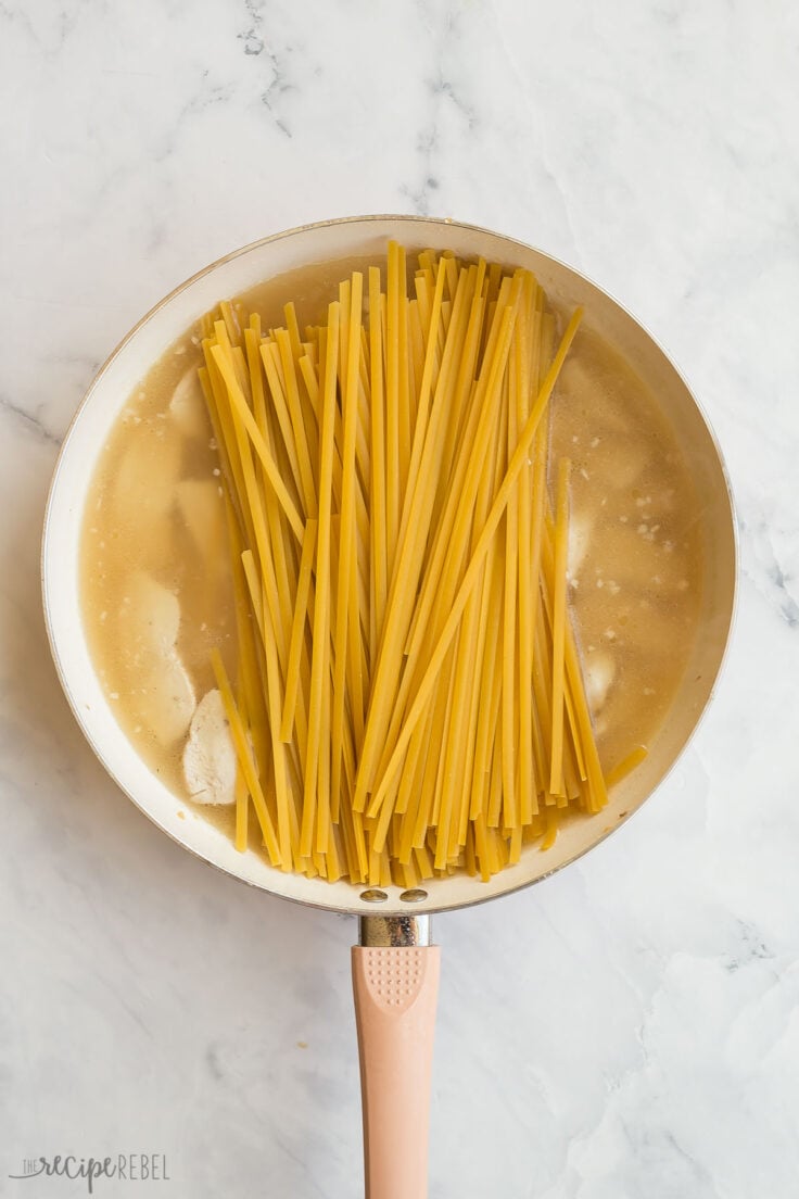 dry fettuccine noodles added to chicken and broth in white skillet