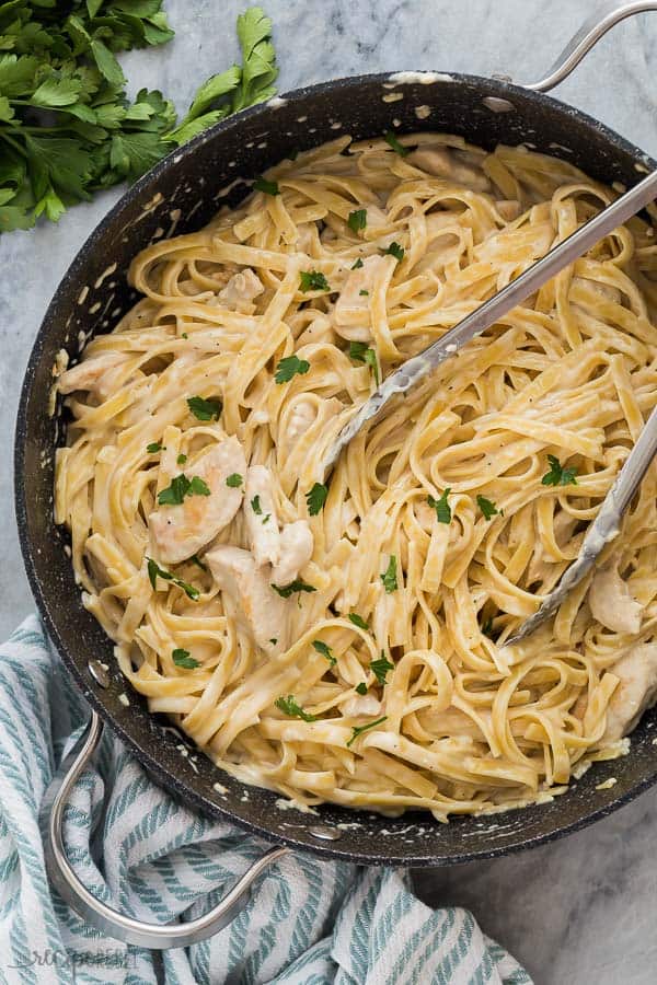 chicken fettuccine alfredo overhead in black skillet with tongs stuck into pasta