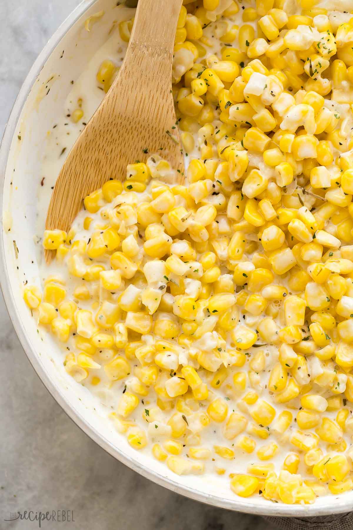 wooden spoon scooping creamed corn from skillet.