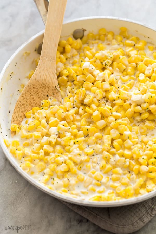 creamy corn in pan with wooden spoon on marble background