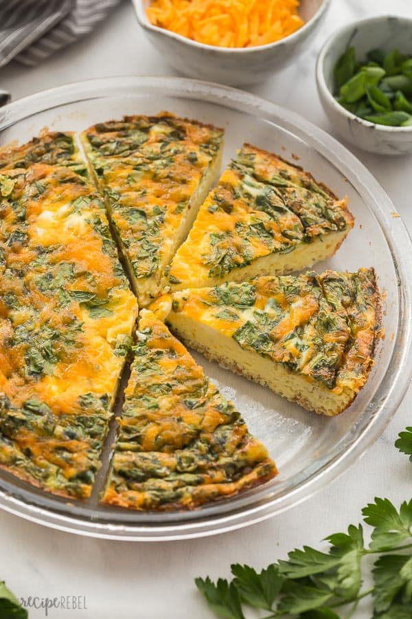 crustless quiche in pan sliced with cheese and spinach in background